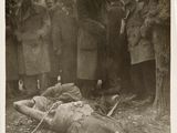 an old black and white photo of a group of people standing around a dead man