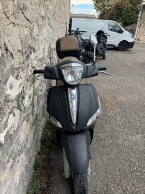 un scooter garé près d'un mur de pierre, avec une camionnette en arrière-plan