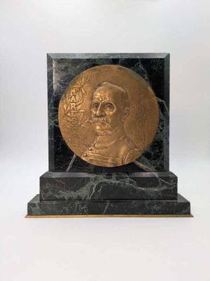 une image représentant un médaillon en or orné du visage d'un homme, posé sur un socle en marbre