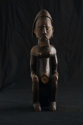 une vieille statue en bois représentant un homme assis sur un fond noir
