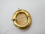 une broche en or munie d'une épingle, posée sur une surface blanche