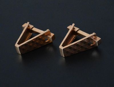 une paire de boucles d'oreilles en forme de triangle en or sur un fond noir