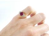 a woman ' s hand holding a ring with a red stone on it