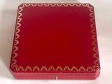 une boîte rouge ornée d'une bordure dorée, posée sur un fond blanc