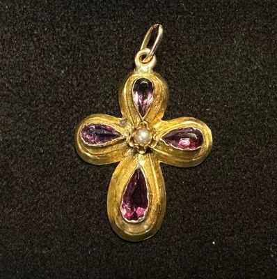 an image of a gold cross with pink stones on a black surface