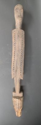 sculpture en bois représentant un homme tenant un couteau, sur un mur gris