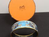 une boîte orange sur laquelle repose un bracelet bleu et or, posée sur une table noire