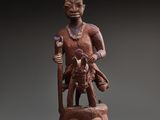 une statue en bois représentant un homme coiffé d'un chapeau et muni d'un bâton