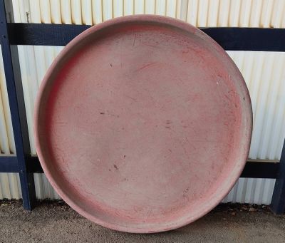 a large pink plate sitting on the ground near a fence
