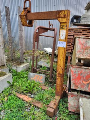a rusted crane sitting in the grass next to a pile of junk