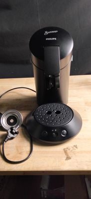 a coffee maker sitting on a wooden table with a cup of coffee