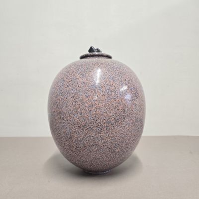un vase violet avec un couvercle noir posé sur une table