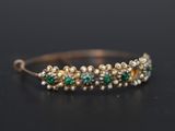 a close up of a gold bracelet with pearls and emeralds