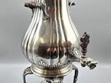 une cafetière ancienne en argent posée sur un socle, sur fond gris