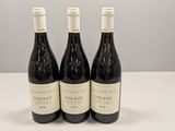 trois bouteilles de vin rouge sont posées sur une table devant un mur blanc