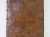 an old book with a brown cover sitting on a white surface
