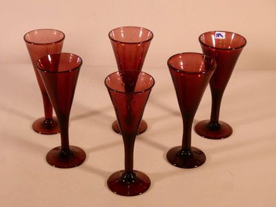 four red wine glasses are lined up on a white surface