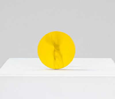 une sculpture jaune posée sur un socle blanc