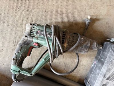 Une photo d'une perceuse filaire est posée par terre à côté d'une feuille de papier.