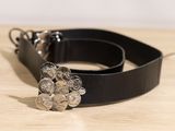 ceinture en cuir noir avec une boucle en forme de fleur en métal argenté posée sur une surface en bois
