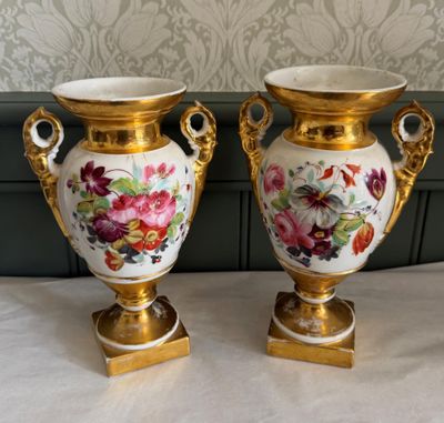 Deux vases sont posés sur une table, avec un papier peint en arrière-plan.