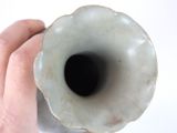 a hand holding a white vase with a black hole in it