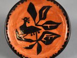 une assiette orange et noire ornée d'un oiseau, posée sur un socle