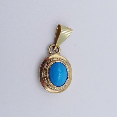 un gros plan d'un pendentif en or et en turquoise sur une surface blanche