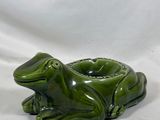 une grenouille en céramique verte posée sur un tissu blanc
