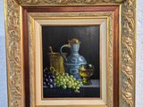 un tableau représentant des raisins et une cruche en argent posé sur un chevalet
