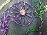purple and green beaded pillow with a flower design on top of it