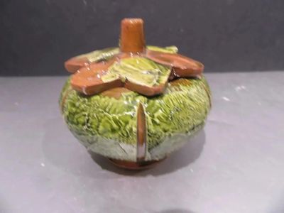 a green and brown vase with a flower on top of it