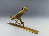 un télescope ancien en laiton posé sur un socle, sur fond blanc