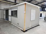 un petit bâtiment blanc situé dans un entrepôt, dont la porte est ouverte