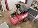 a red air compressor sitting on the floor in a garage