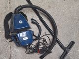 un aspirateur bleu et un tuyau noir posés par terre