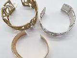 three gold and silver cuff bracelets, one with an open design, the other with an open design