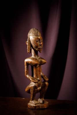a wooden statue sitting on top of a table next to a purple curtain