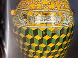 a picture of a yellow and green vase in a glass case