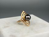 une photo d'une perle noire et d'une bague en or posées sur un bloc de marbre