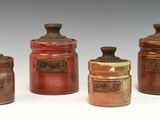 four brown jars with lids are lined up on a white surface