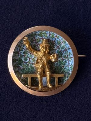 a gold brooch with a picture of a man holding a tennis racquet