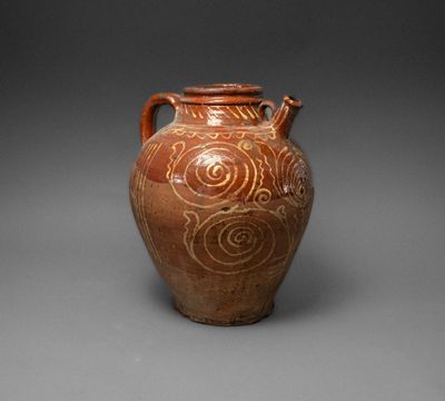 an old brown vase with swirl designs on it on a gray surface