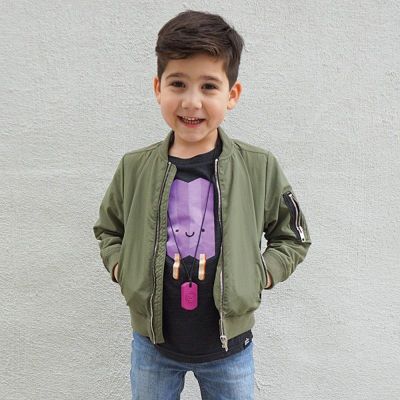 a young boy standing in front of a white wall wearing a green jacket