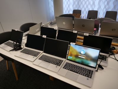 Plusieurs ordinateurs portables sont posés sur une table devant une rangée de chaises