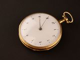 a gold pocket watch with a white face on a black surface