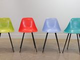 Quatre chaises en plastique colorées sont alignées contre un mur blanc.