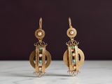 une paire de boucles d'oreilles en or ornées de perles et d'émeraudes, posées sur une surface en marbre