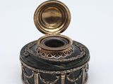 a small black box with a gold lid on a white surface