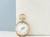 a small gold pocket watch sitting on a marble block